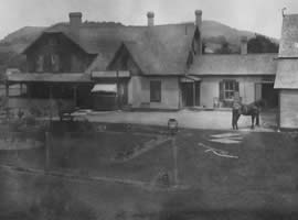 historic black and white photograph of two tone house with porch and awnings with a horse and lantern post out front