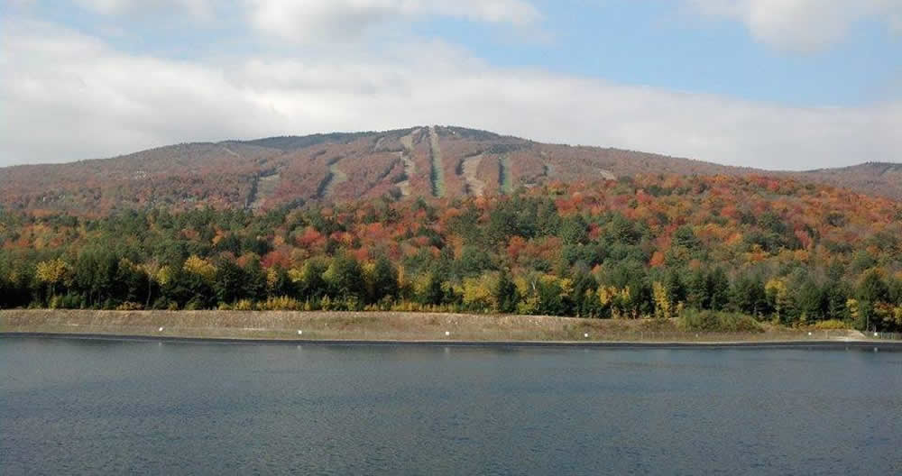 autumn colors of reds and greens on a ski mountain behind a calm lake.