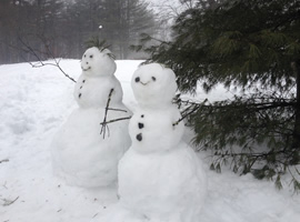 two snow men in front of pine tree