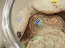 looking down into a glass cookie jar stacked full with golden brown cookies with M&M candies