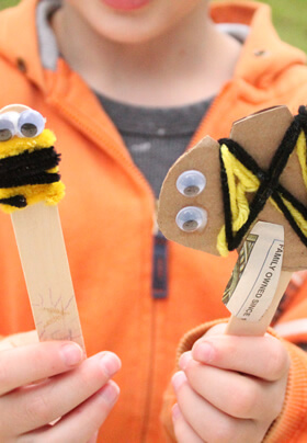 close up of young hands holding two different child crafts, both with googly eyes and yellow and black yarn or pipe cleaners fastened to resemble a honeybee