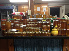 Maybe 100 jars of honey of various sizes and shapes all stacked on top of one another sitting on top of a black stone kitchen counter with country wooden cabinets in the background