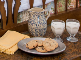 speckled gray and blue pottery pitcher with two glasses of milk and a pewter tray of cookies on an antique wooden trunk